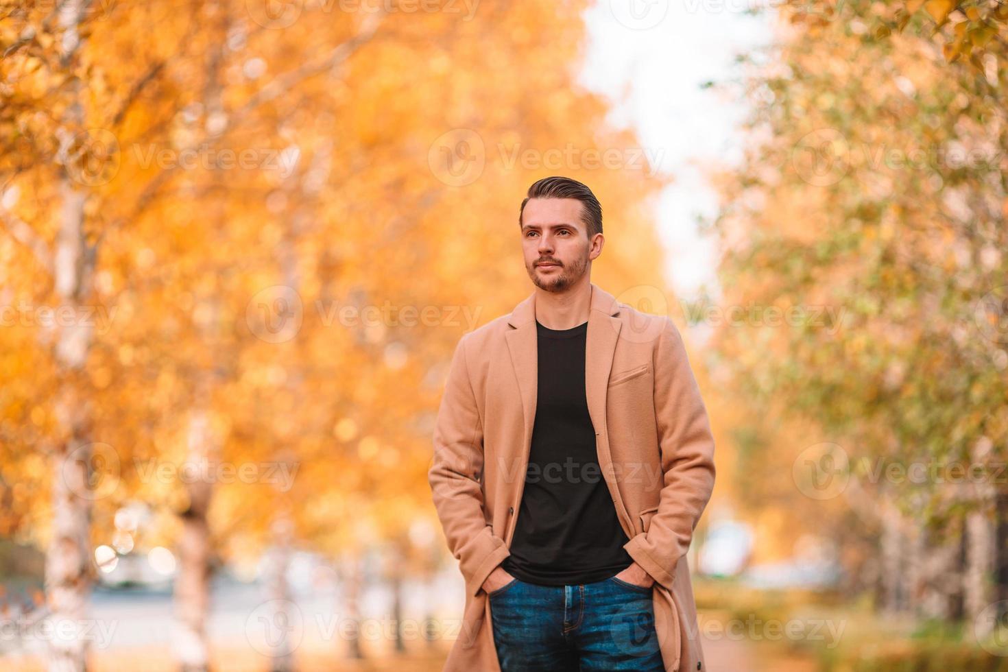 Young man drinking coffee with phone in autumn park outdoors photo