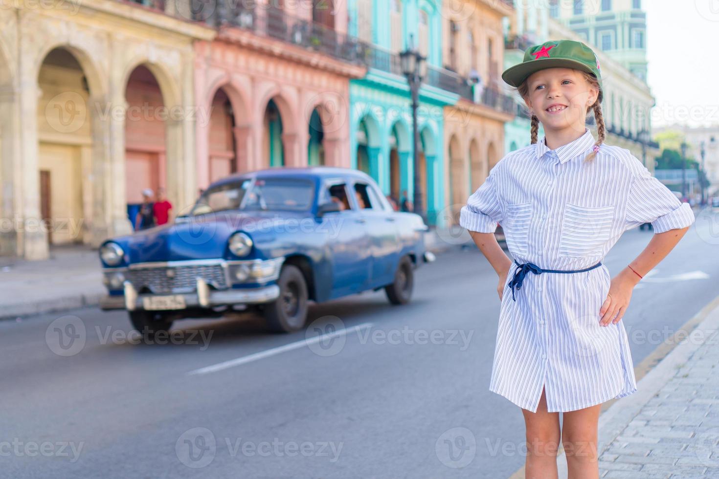 adorable niña en zona popular en la habana vieja, cuba. retrato de niño fondo vintage coche americano clásico foto