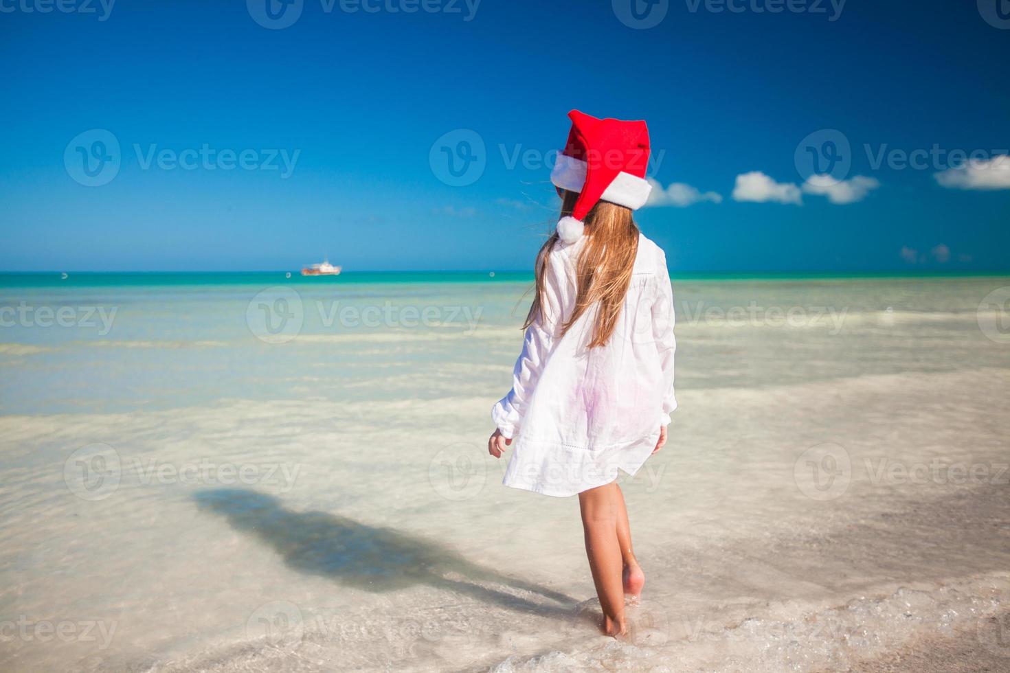 Little cute girl in red hat santa claus on the beach photo