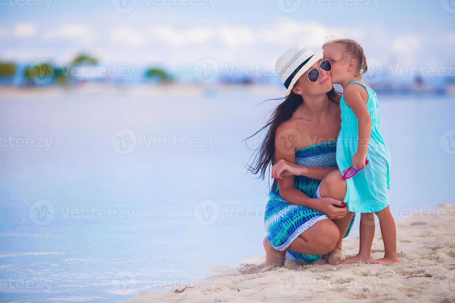 Little girl kissing her beautiful mother on a white tropical beach photo