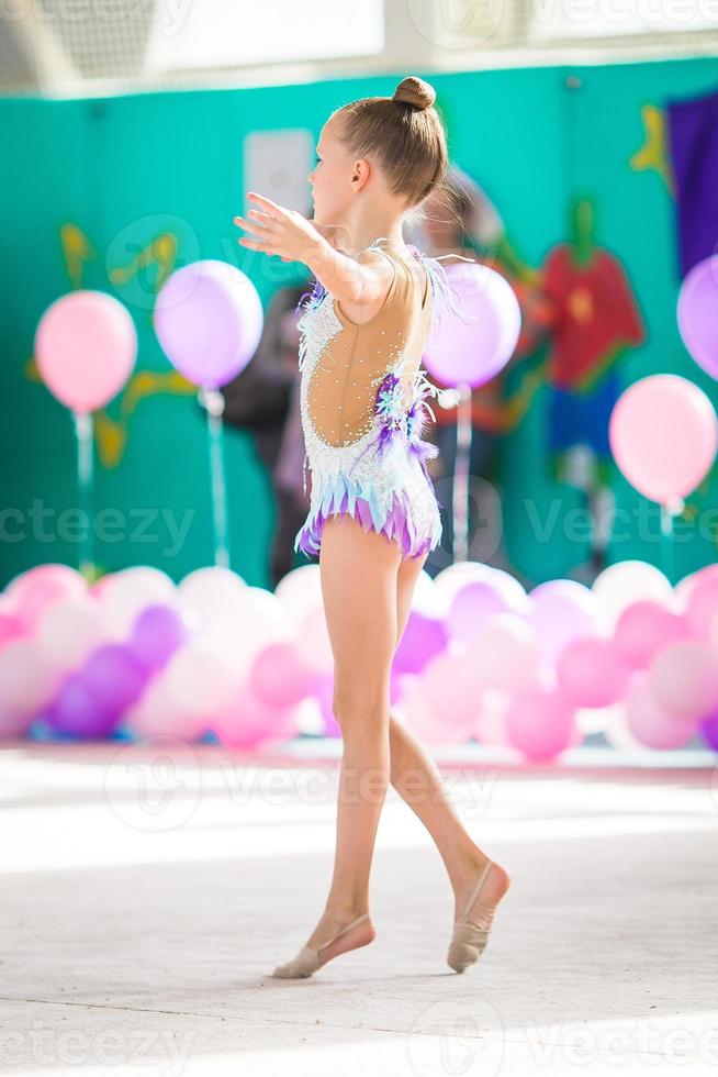 pequeña y hermosa gimnasta en la alfombra. adorable gimnasta participa en competiciones de gimnasia rítmica foto