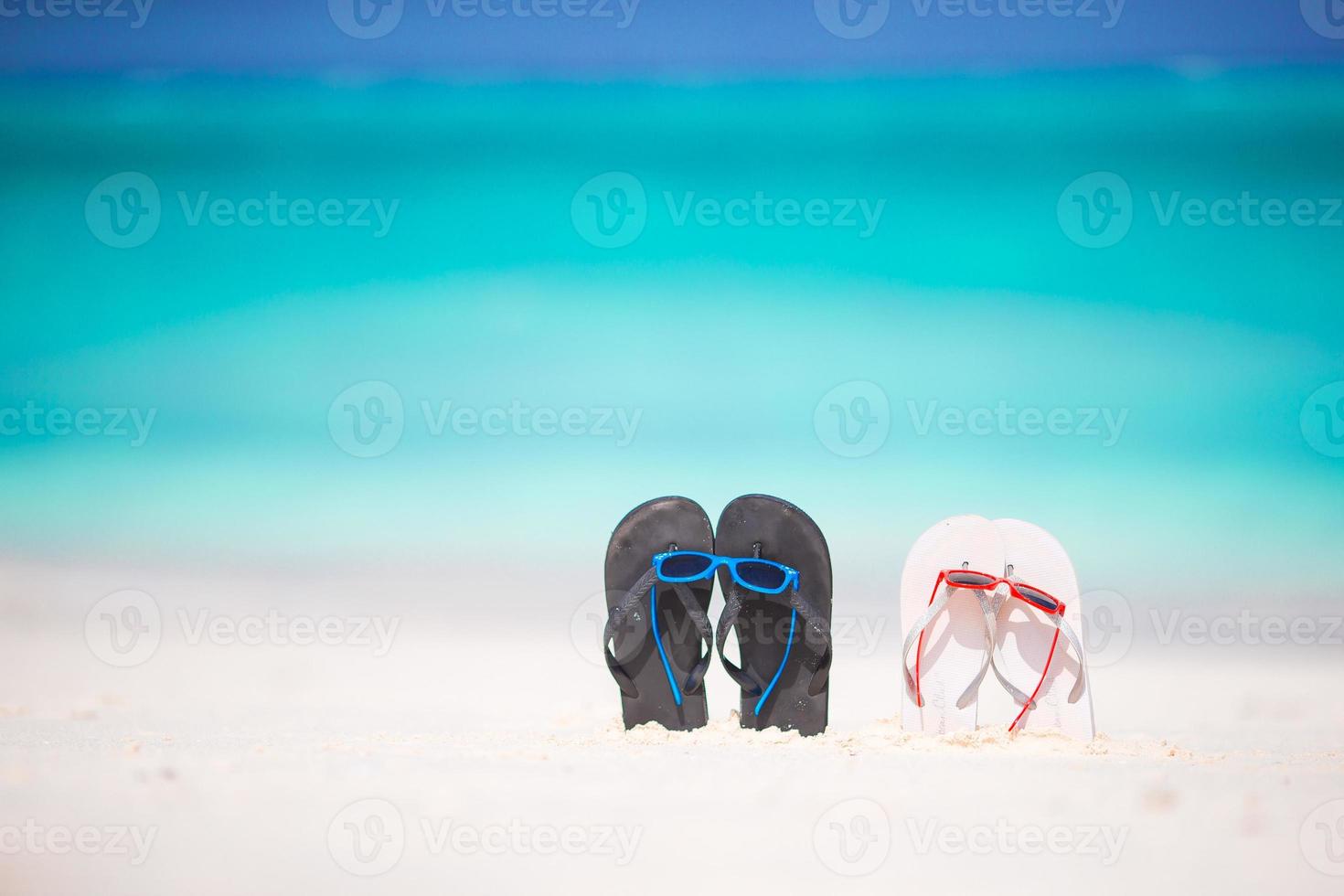 Summer flip flops with sunglasses on white beach. Closeup beach accessories. photo