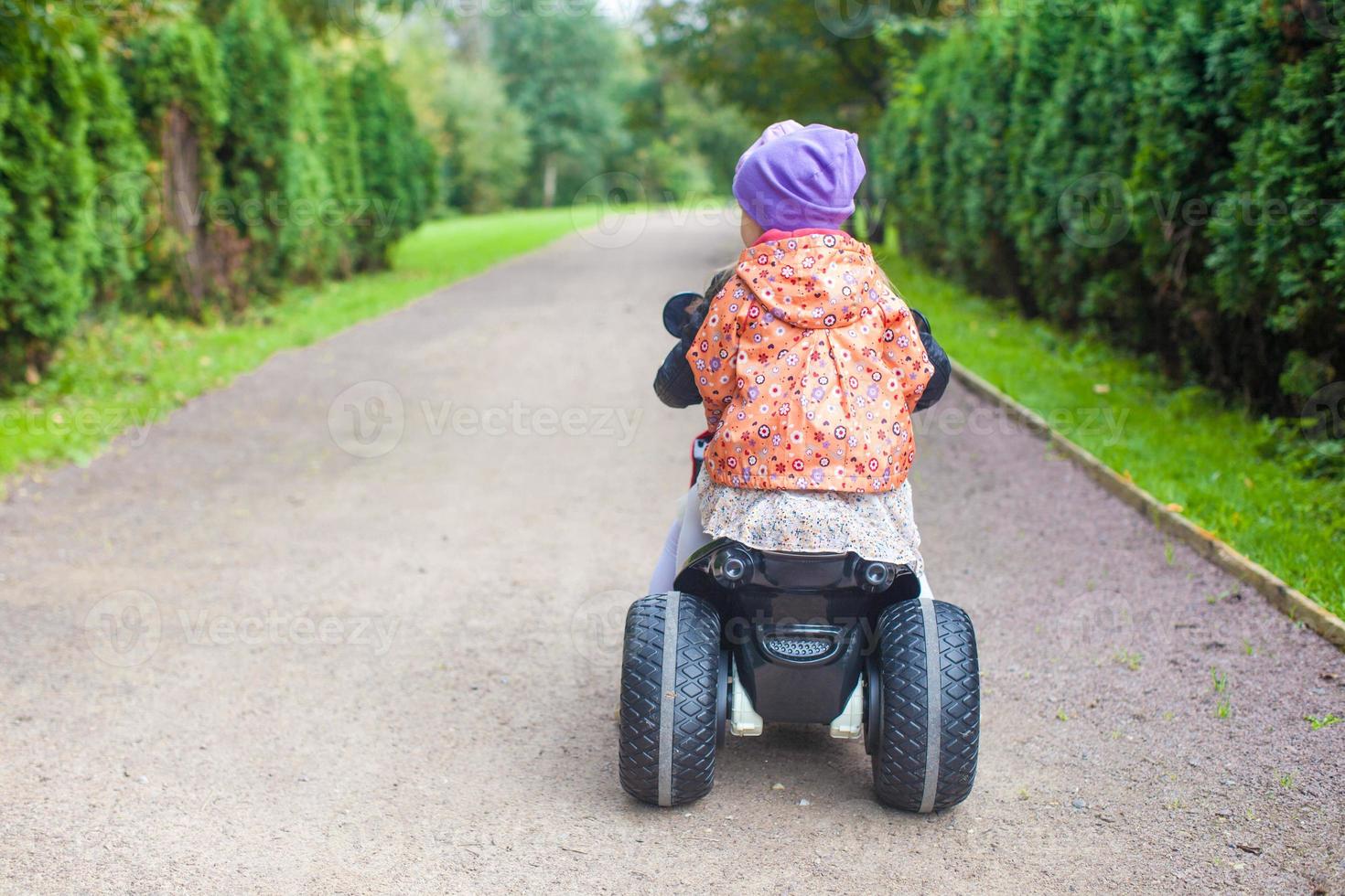 Back view of adorable little girls ride a motorbike in green park photo