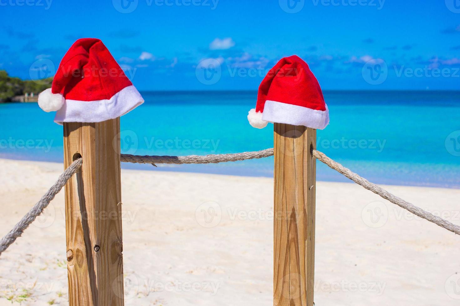 Two red Santa hats on fence at tropical white beach photo