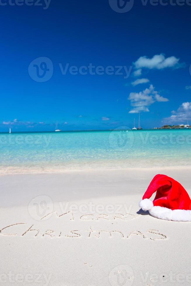 feliz navidad escrita en una playa tropical de arena blanca con sombrero de navidad foto