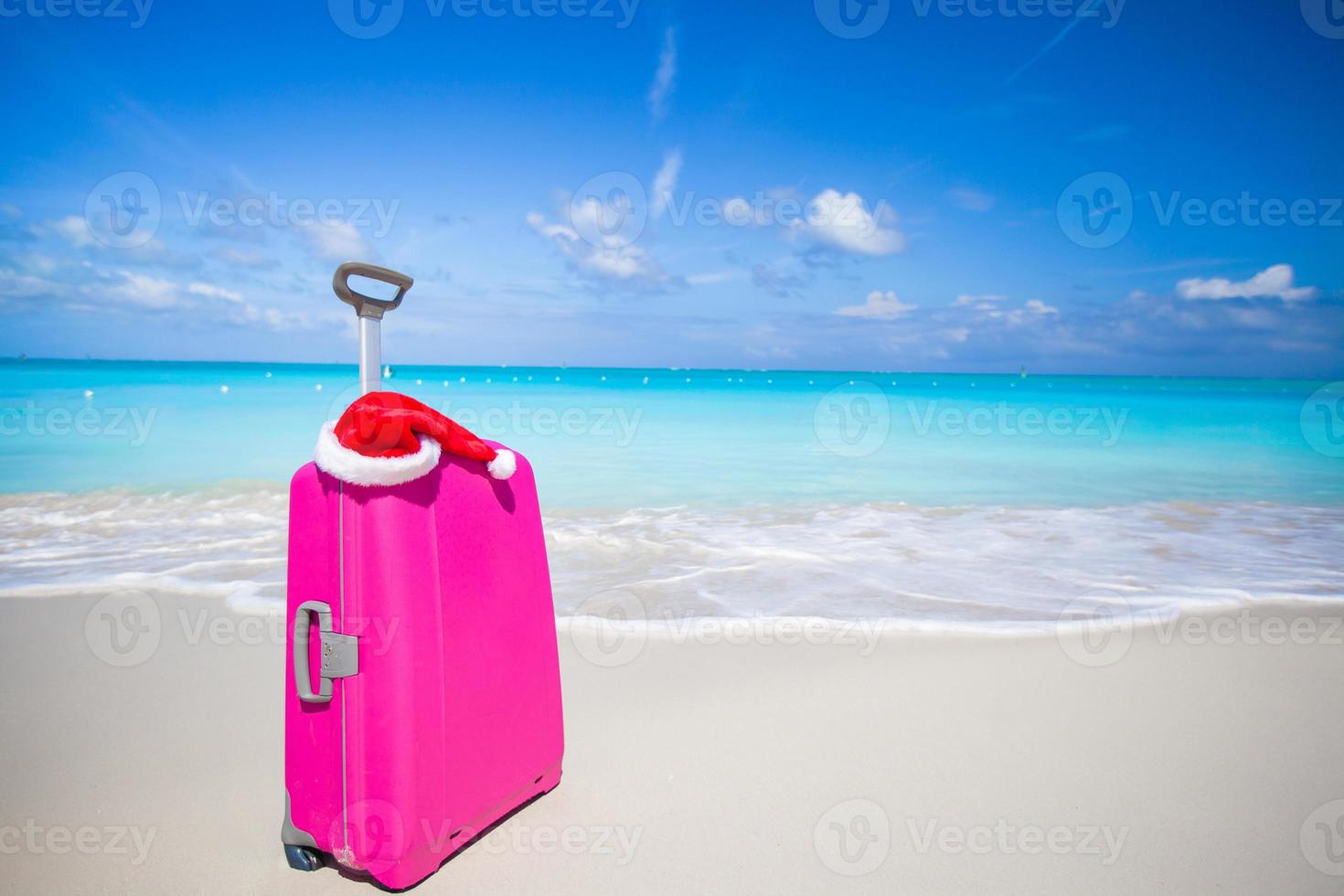 Closeup of pink suitcase and Santa Claus hat on beach photo