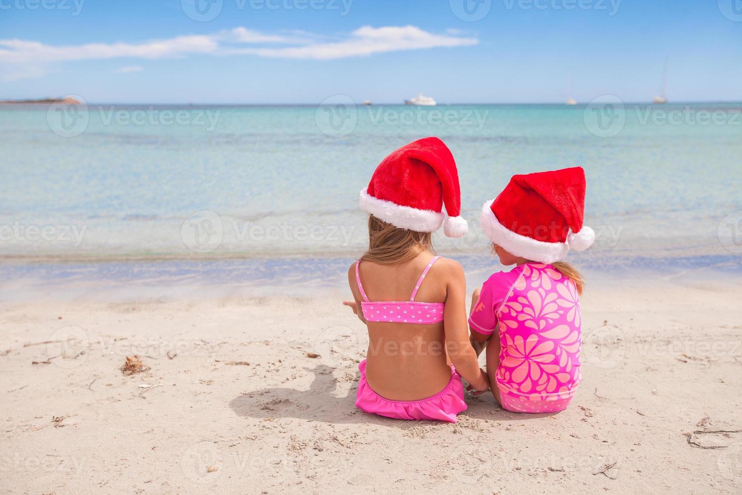 Little adorable girls in Santa hats during beach vacation photo