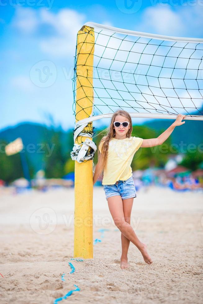 Little adorable girl playing beach volleyball with ball. Sporty family enjoy beach game outdoors photo