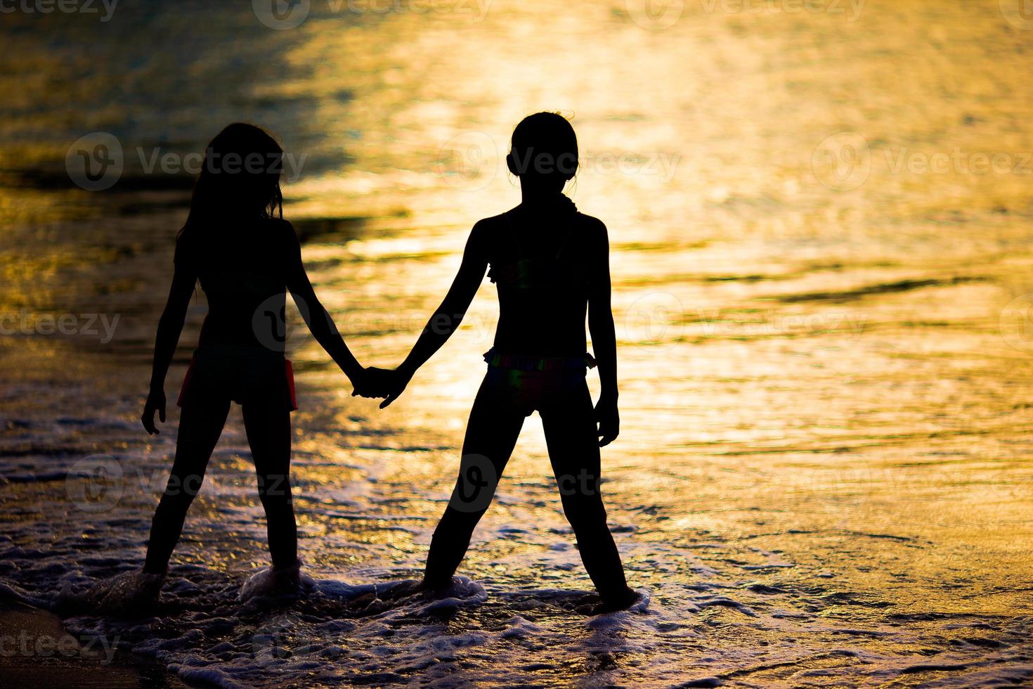 niñas adorables en la playa con una hermosa puesta de sol colorida foto