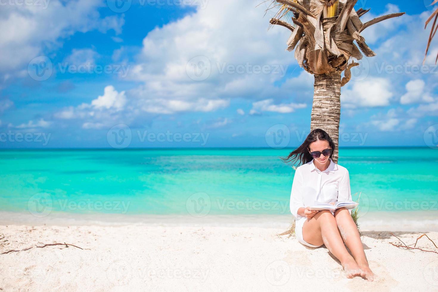 Young woman reading on tropical white beach near palm tree photo