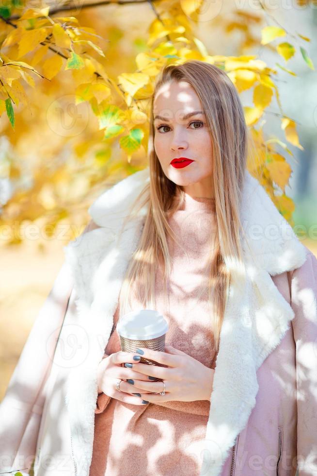 Fall concept - beautiful woman drinking coffee in autumn park under fall foliage photo