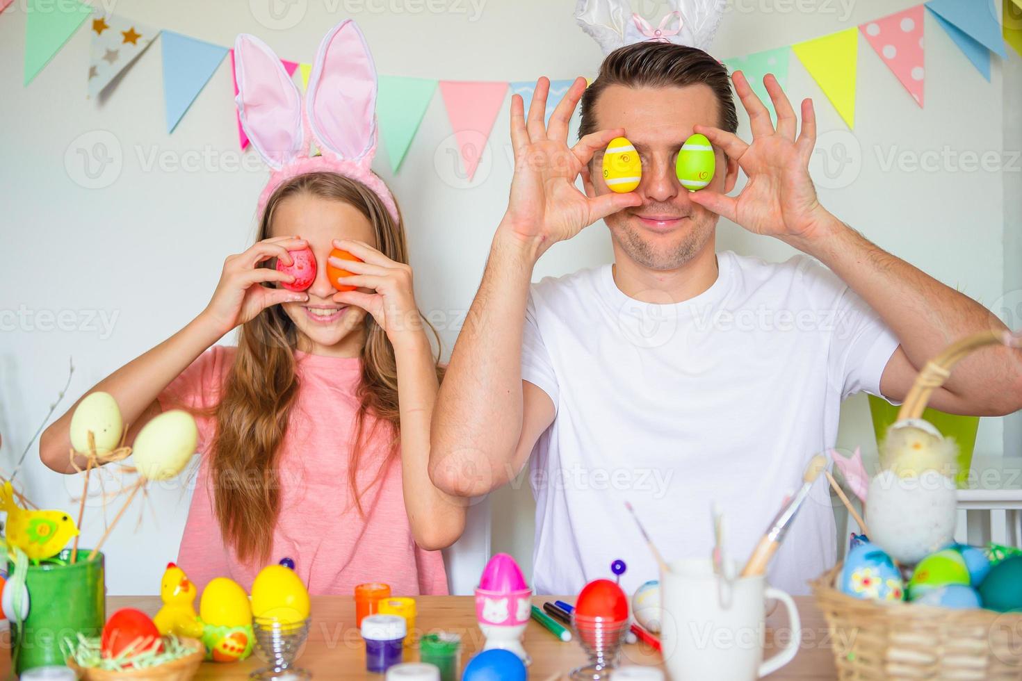 Father and his little daughter painting eggs. Happy family preparing for Easter. photo