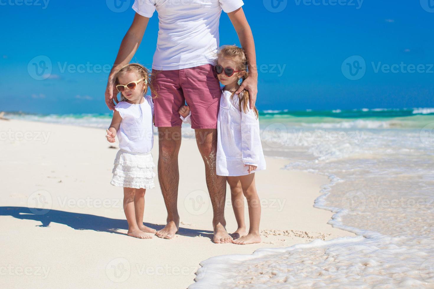 joven padre feliz y pequeñas hijas divirtiéndose en la playa blanca en un día soleado foto