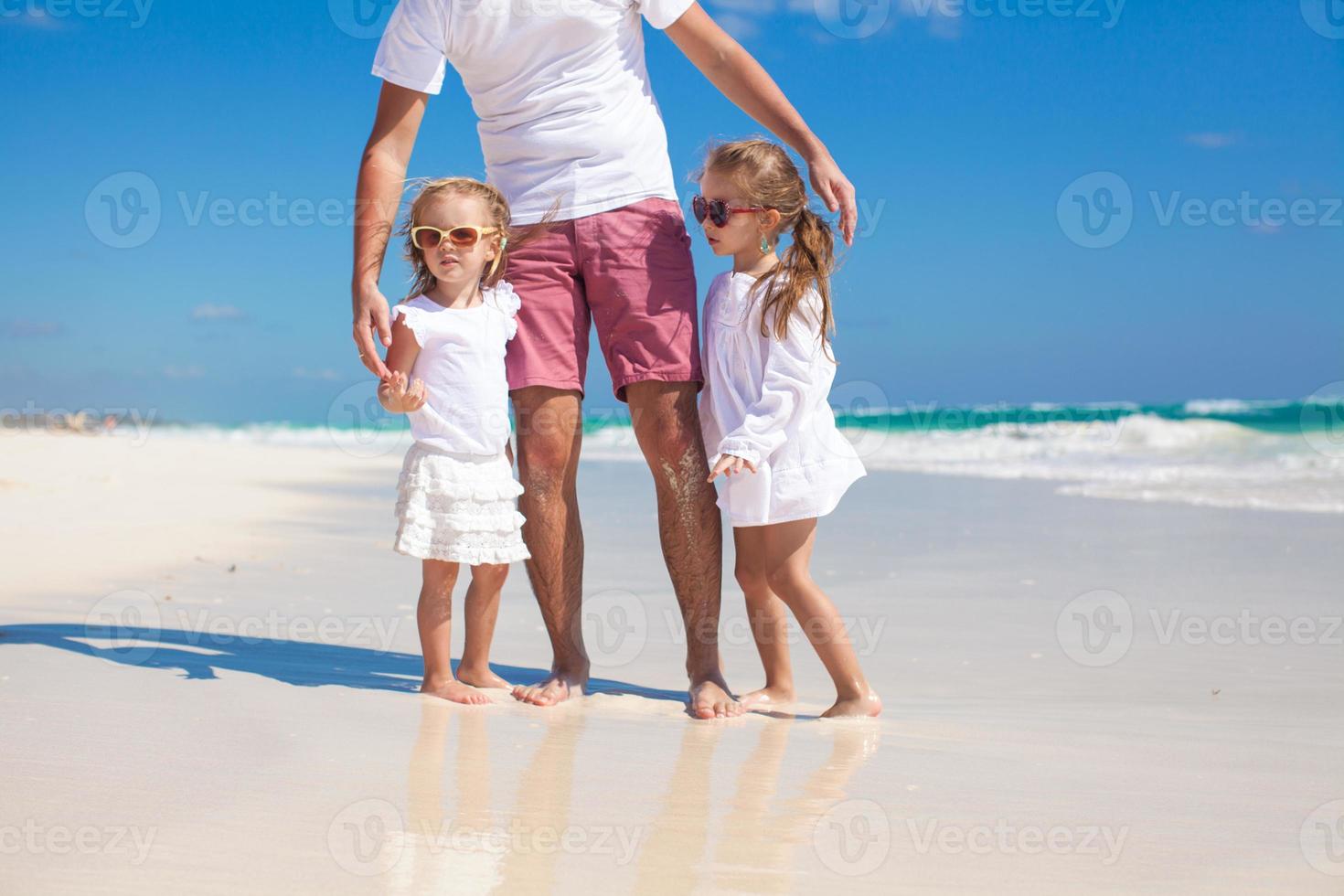 joven padre feliz y pequeñas hijas divirtiéndose en la playa blanca en un día soleado foto