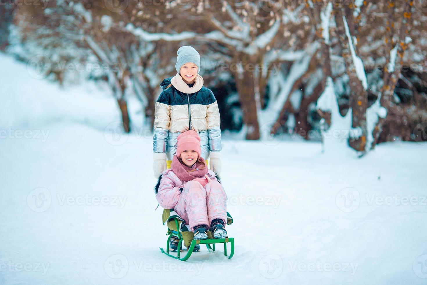 Adorable little happy girls sledding in winter snowy day. photo