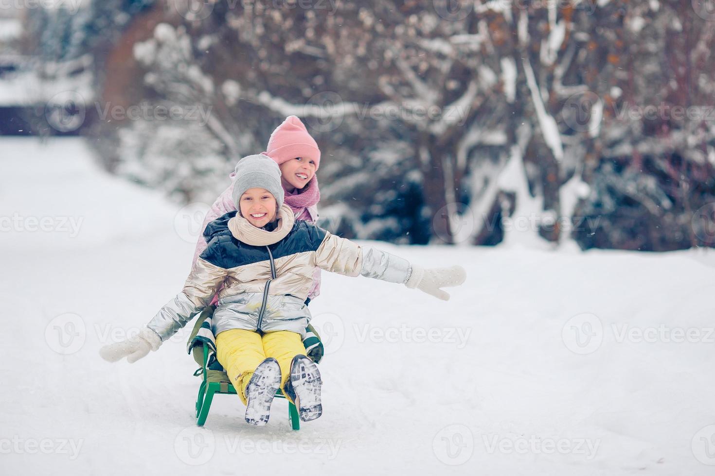 Adorable little happy girls sledding in winter snowy day. photo