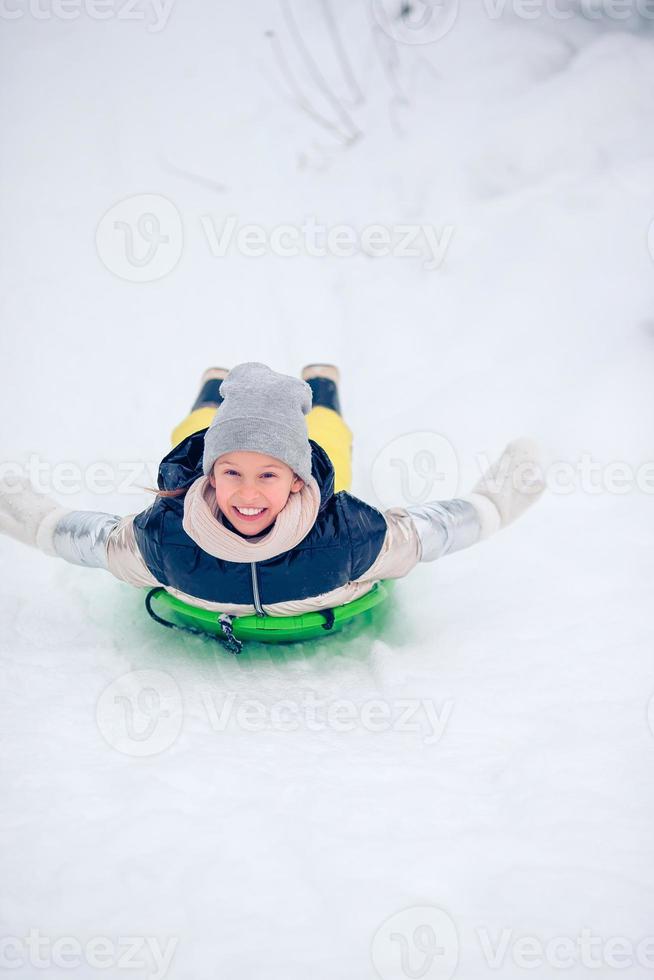Adorable little happy girl sledding in winter snowy day. photo