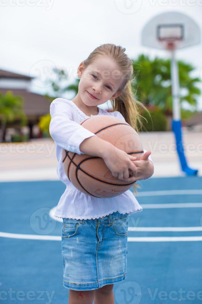 Little girl with basketball on court at tropical resort photo