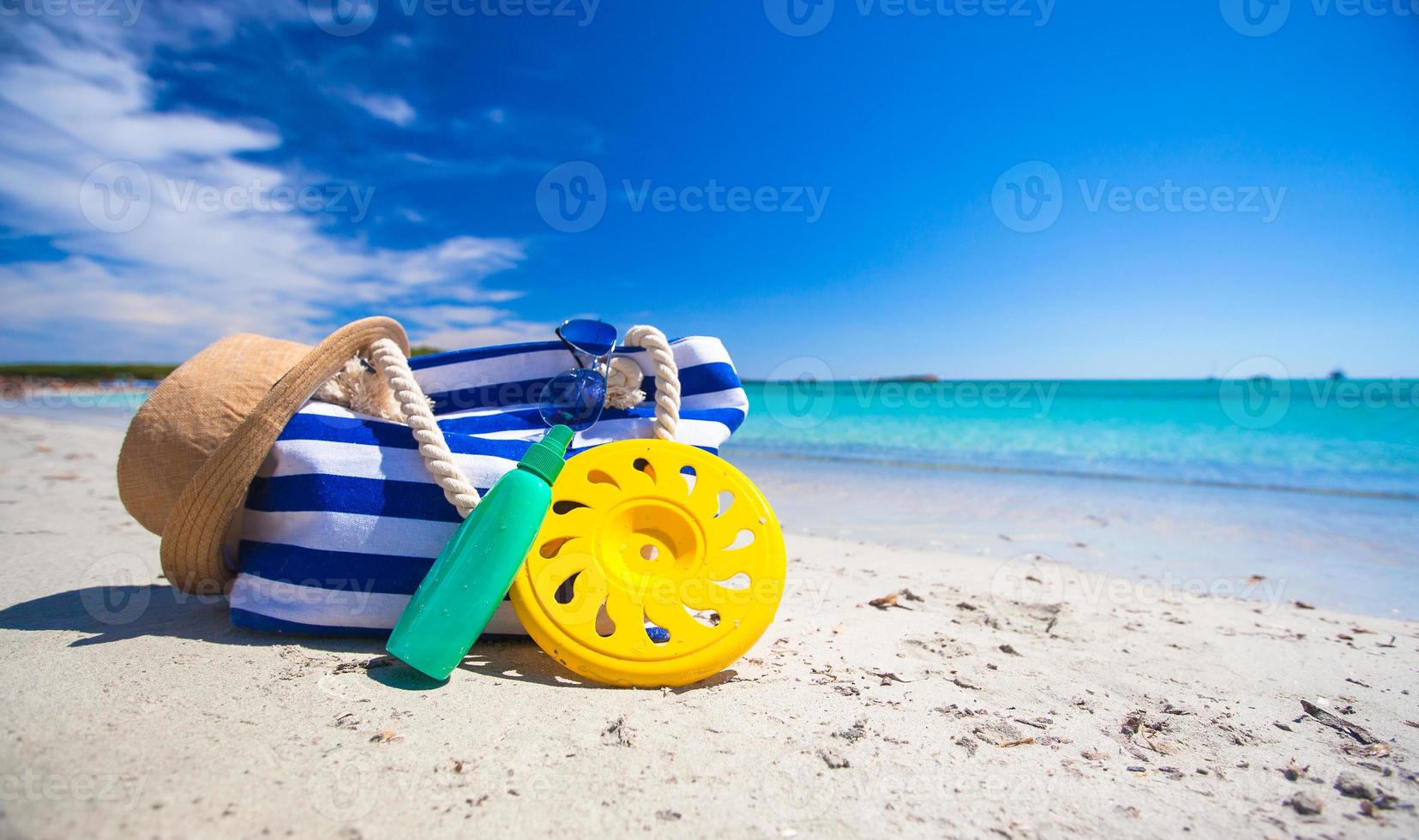 Stripe bag, straw hat, sunblock and frisbee on white sandy tropical beach photo