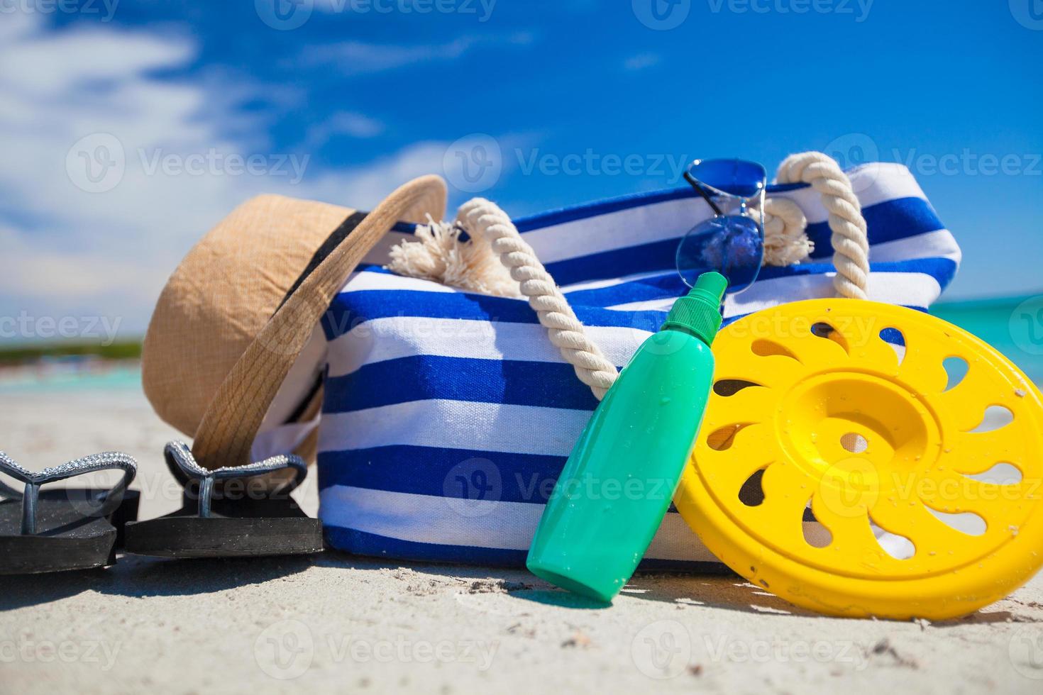 Stripe bag, straw hat, sunblock and frisbee on white sandy tropical beach photo