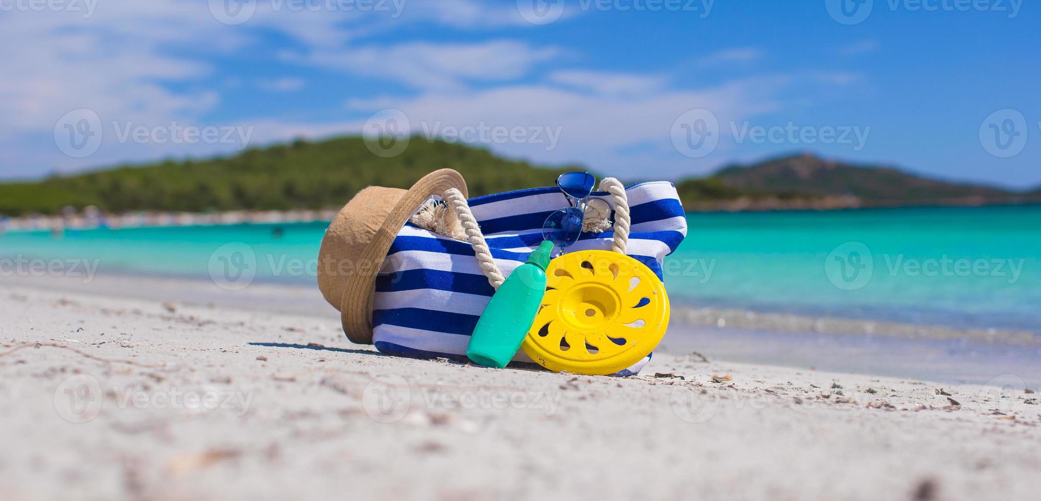 Stripe bag, straw hat, sunblock and frisbee on white sandy tropical beach photo