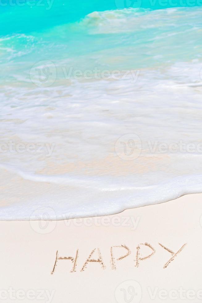 Happy written on sand beach with soft ocean wave on background photo