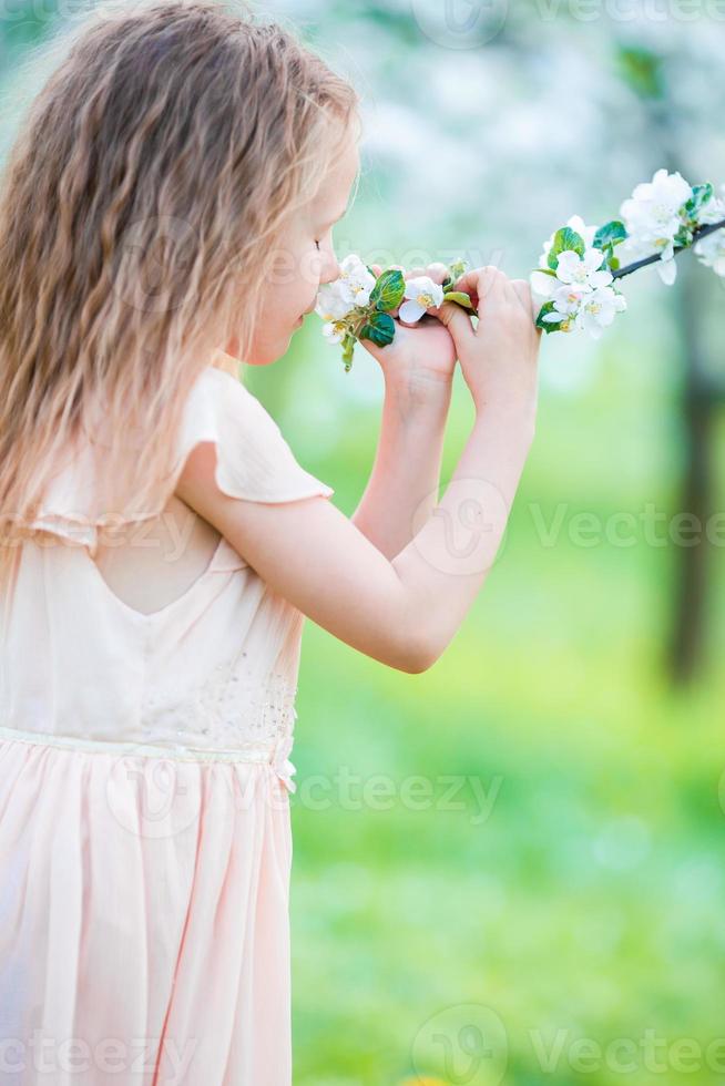 Little beautiful girl enjoying smell of blooming apple tree in a flowering spring garden photo