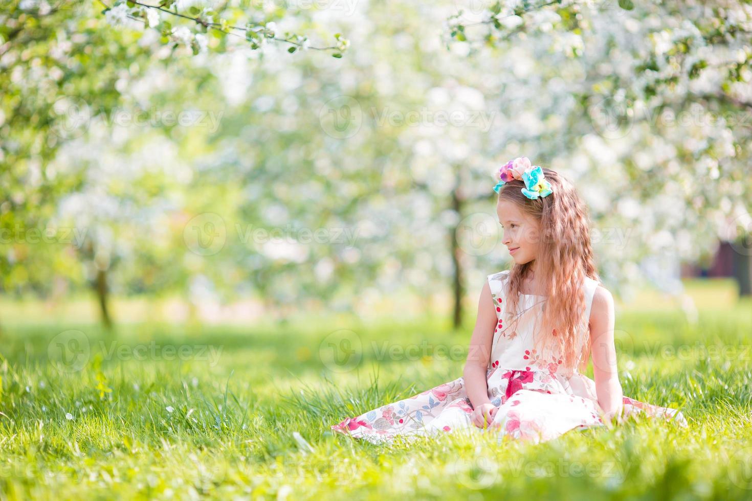 Adorable little girl in blooming apple tree garden on spring day photo