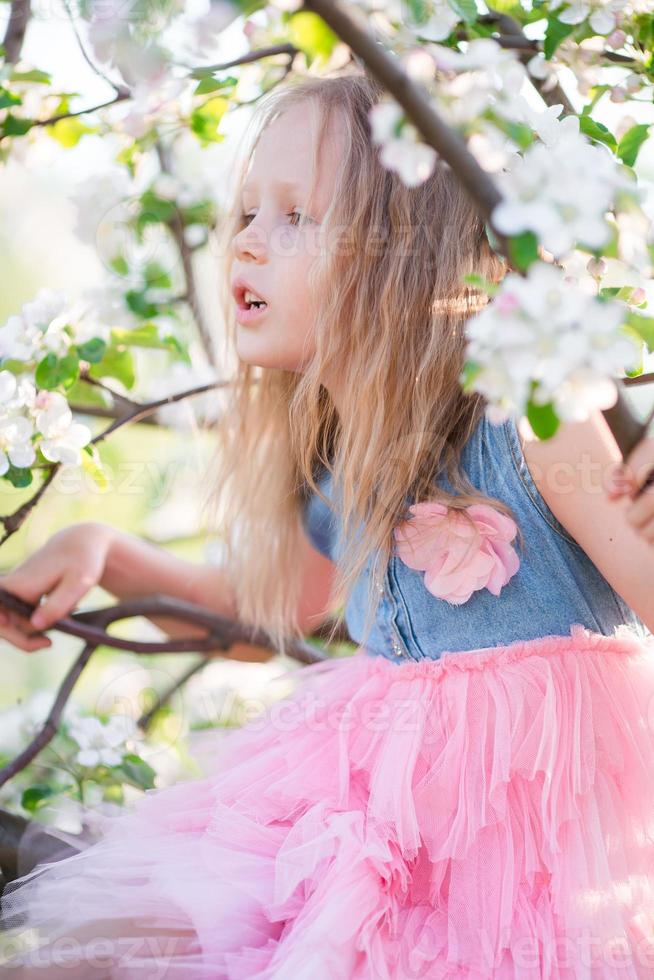 Portrait of beautiful little girl in blooming apple tree garden on spring day photo