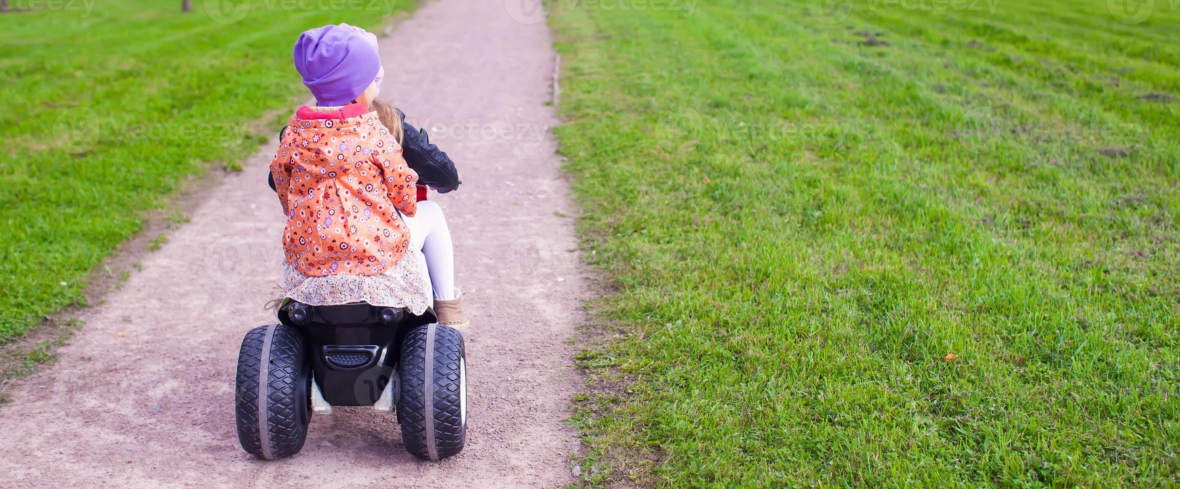 Back view of adorable little girls ride a motorbike in green park photo