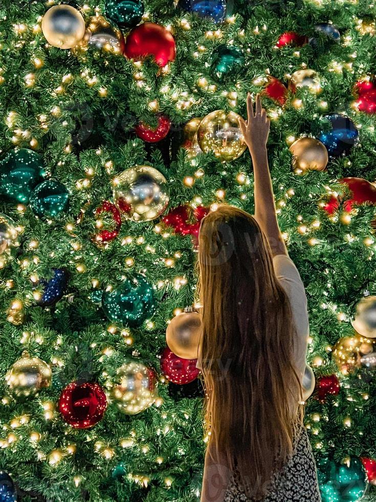 niña en el fondo del árbol de navidad en miami. hermoso árbol de navidad en la zona popular en la víspera de navidad y luces foto