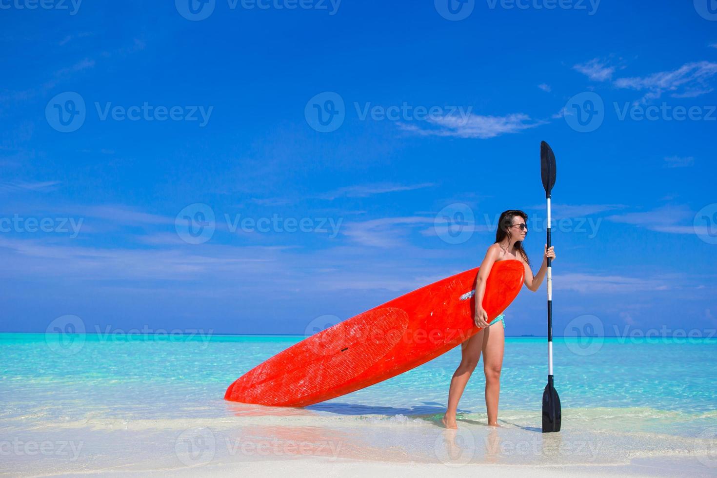 Happy young surf woman at the beach with a surfboard and paddle photo
