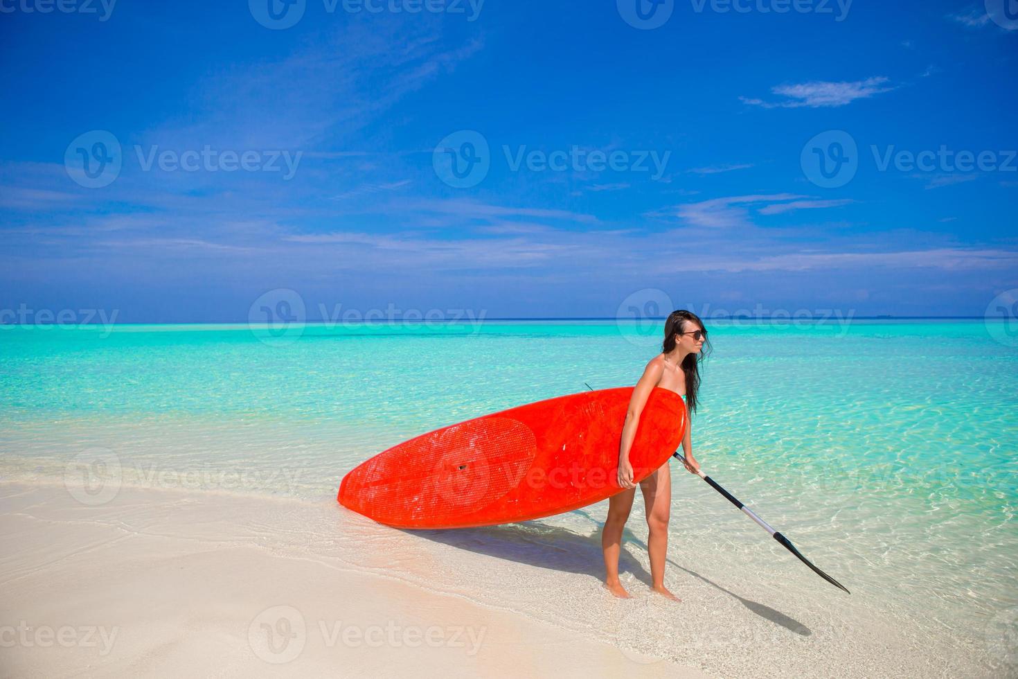 Happy young surf woman at the beach with a surfboard and paddle photo