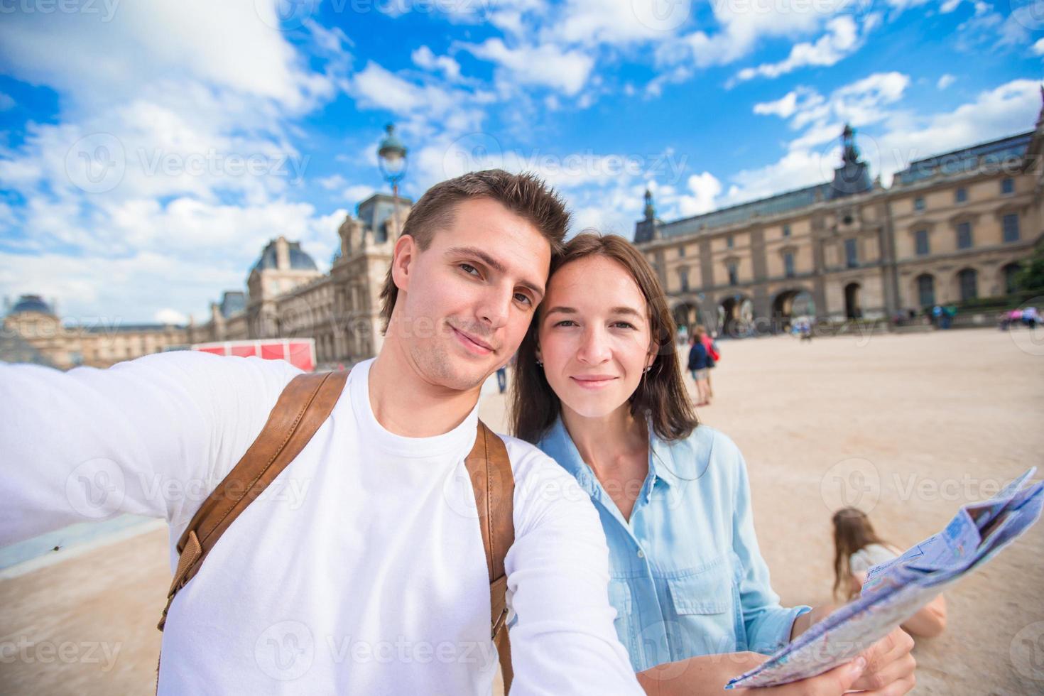 feliz pareja joven con mapa de la ciudad tomando selfie en parís al aire libre foto