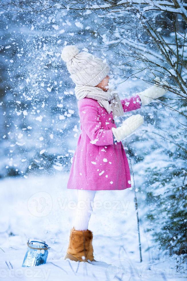 Adorable little girl having fun in the snow on Christmas at winter forest outdoors photo