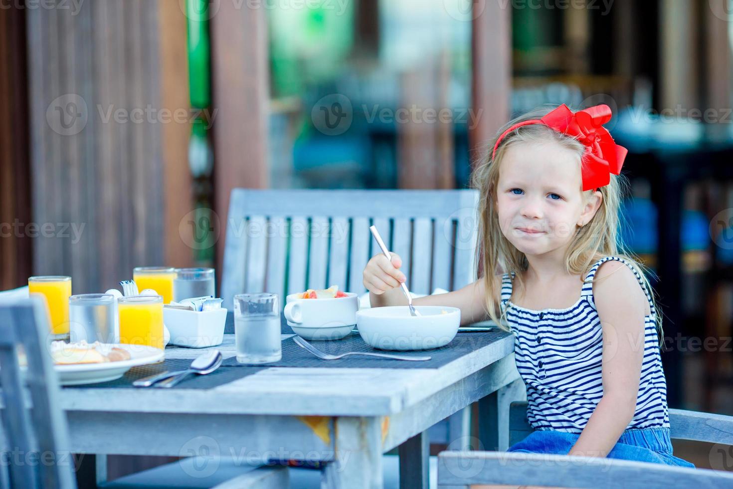 Adorable little girl having breakfast at outdoor cafe photo