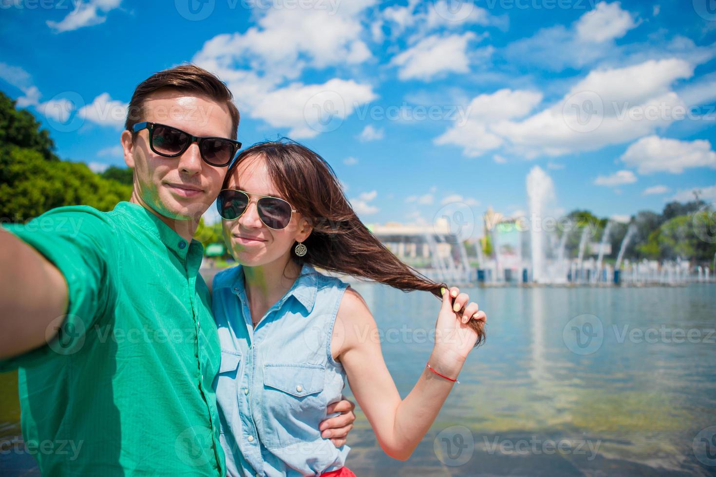 Young tourist couple traveling on holidays in Europe smiling happy. Caucasian girl and man making selfie background of fountain photo