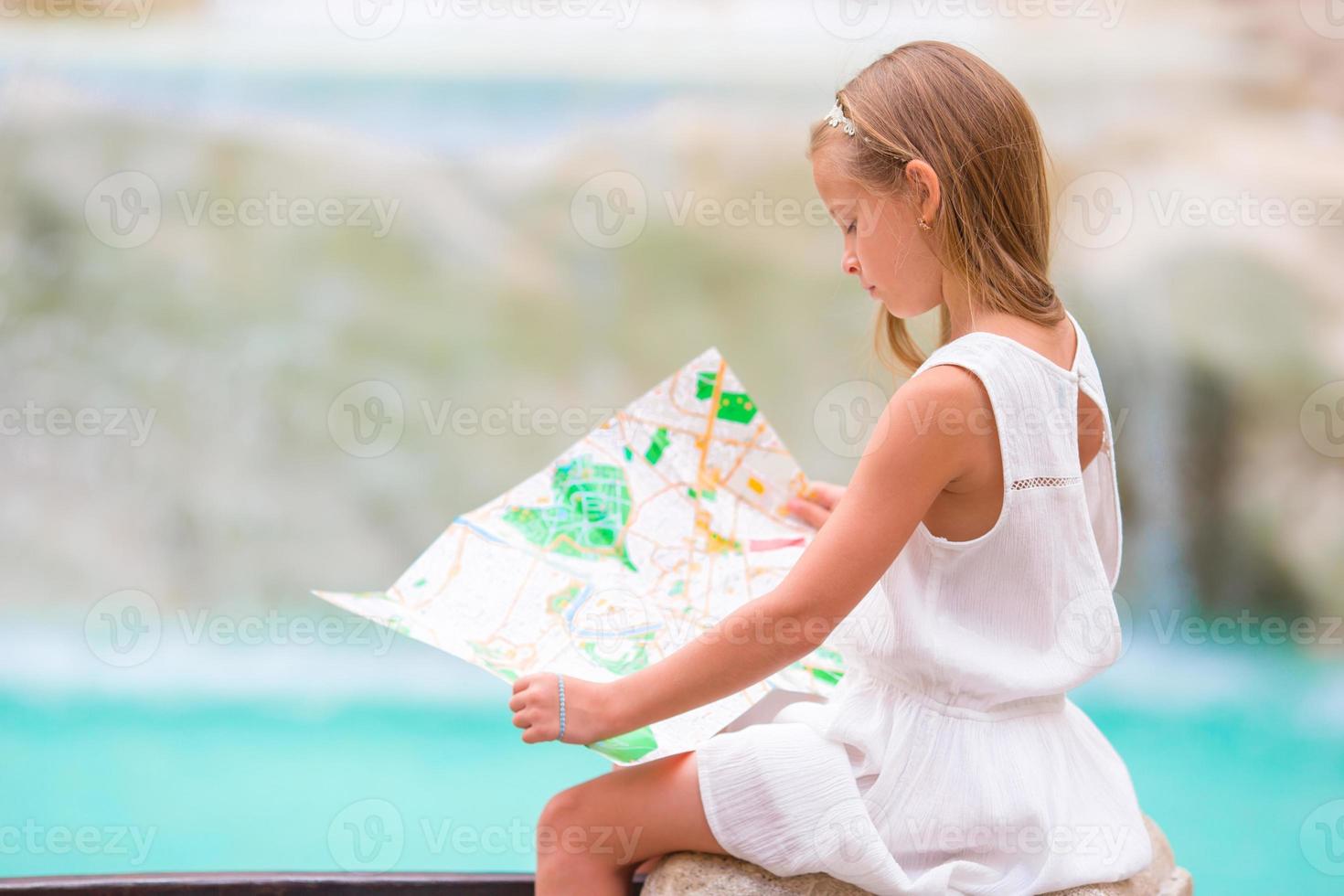 adorable niña mirando el mapa turístico cerca de la fuente de trevi, roma, italia. feliz niño toodler disfruta de vacaciones italianas en europa. foto