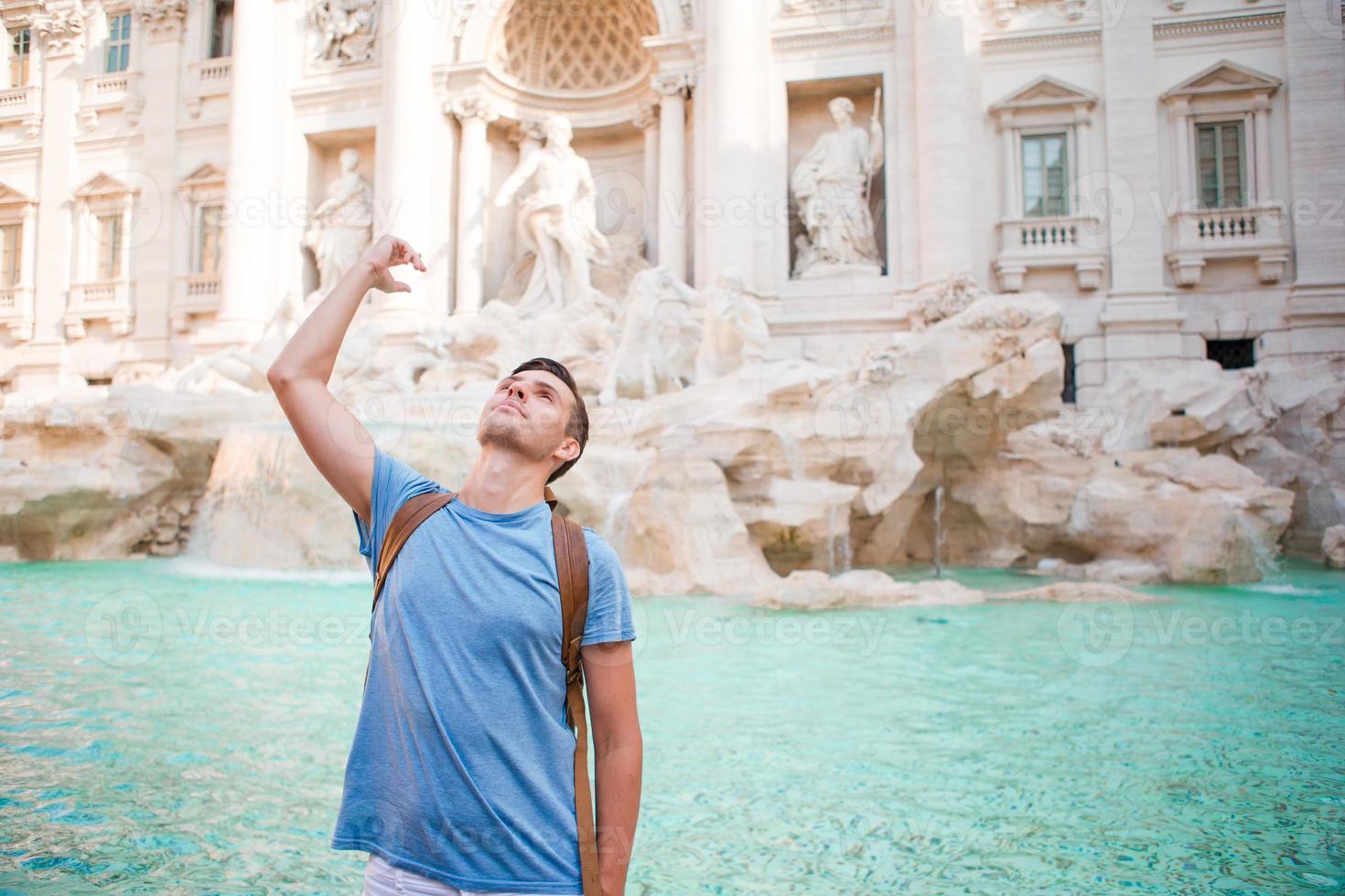 hombre feliz turista tirando monedas en la fuente de trevi, roma, italia para la buena suerte. chico caucásico deseando volver. foto