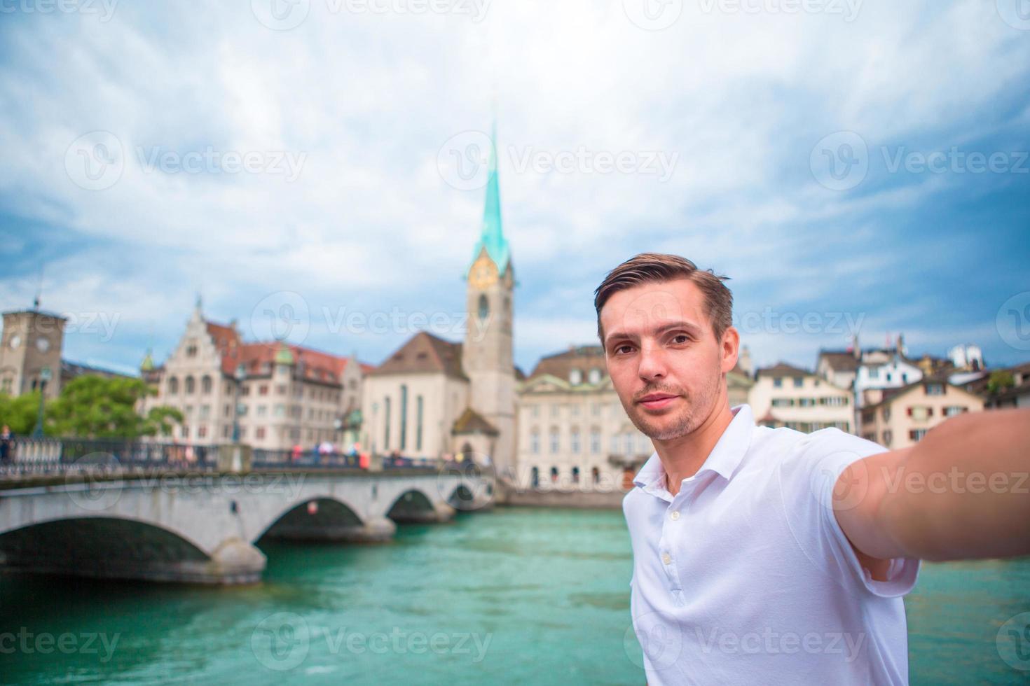 joven tomando selfie antecedentes famosa iglesia fraumunster y río limmat, suiza. foto
