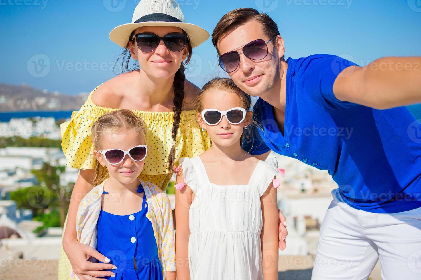 vacaciones familiares en europa. padres e hijos tomando selfie fondo ciudad de mykonos en grecia foto