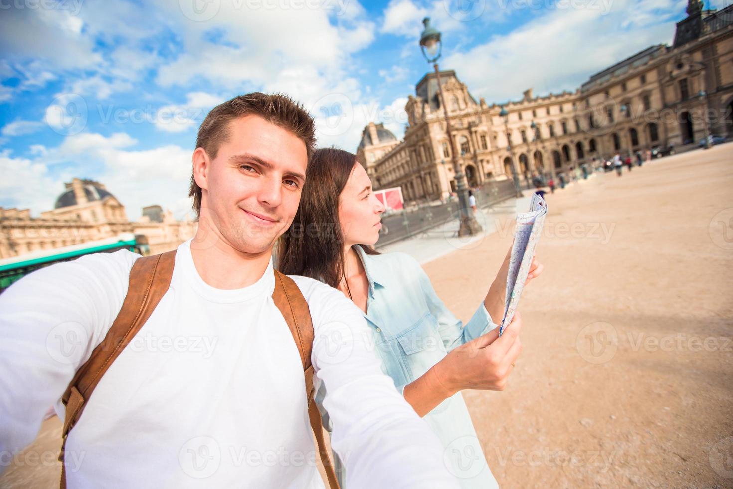 feliz pareja joven con mapa de la ciudad tomando selfie en parís al aire libre foto