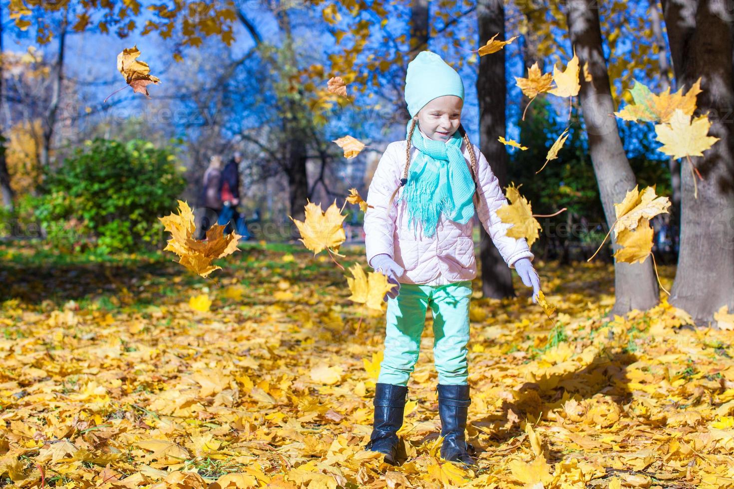 Little funny girl throws autumn leaves in park on fall day photo