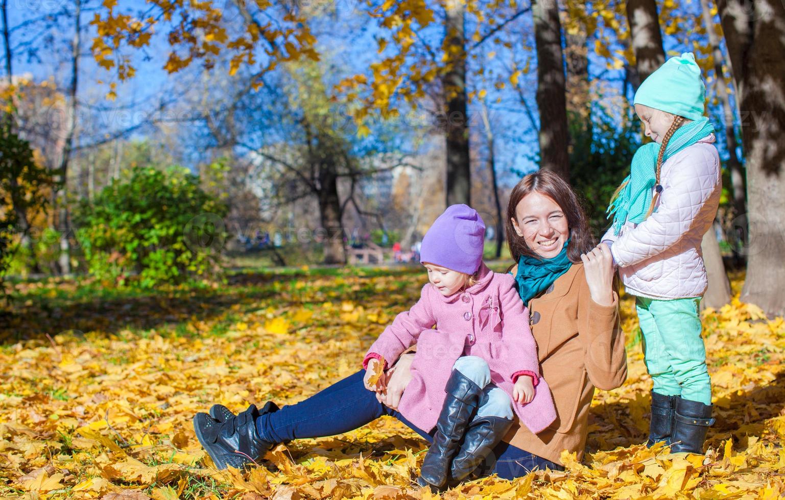 Two adorable girls with his young mom in the park on a sunny autumn day photo