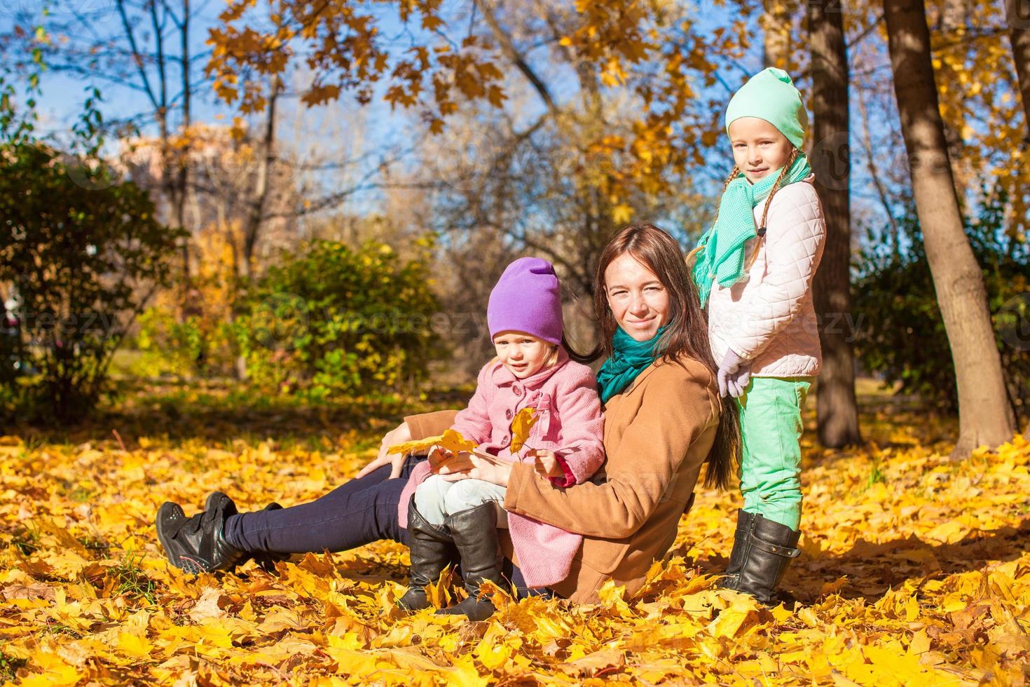 Little girls and young mother in autumn park on sunny warm day photo