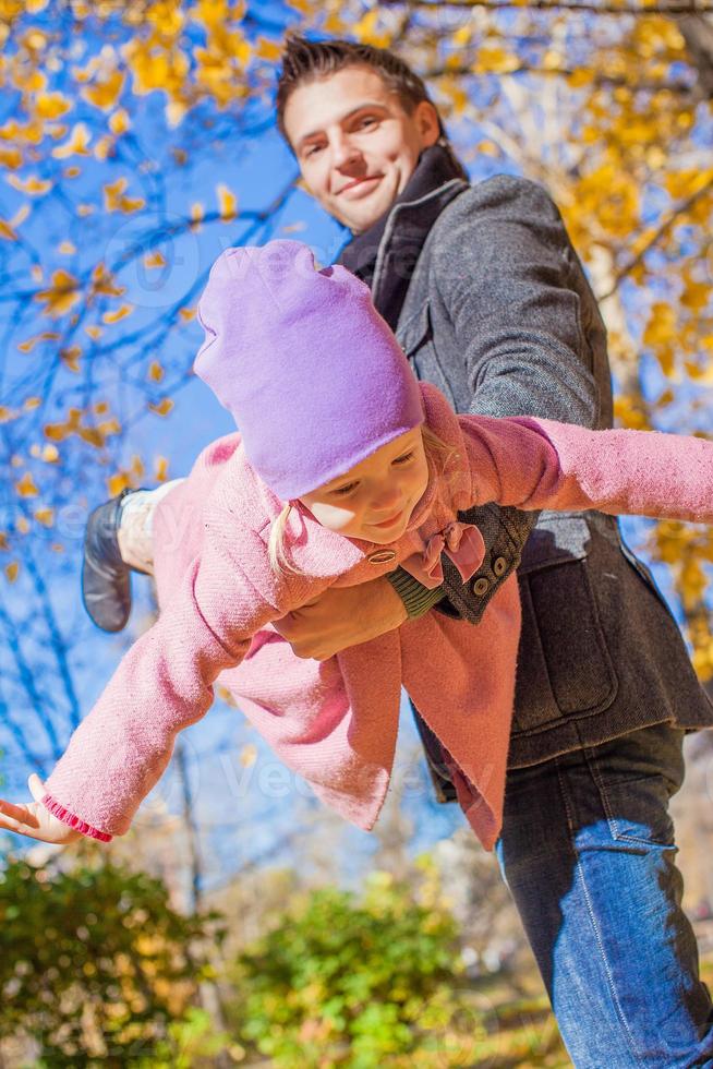 adorable niñita con padre feliz divirtiéndose en el parque de otoño en un día soleado foto