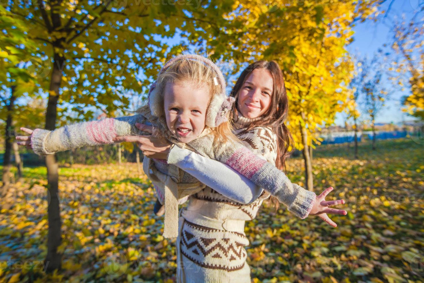 niña adorable y madre joven divirtiéndose en el parque de otoño en un día soleado foto