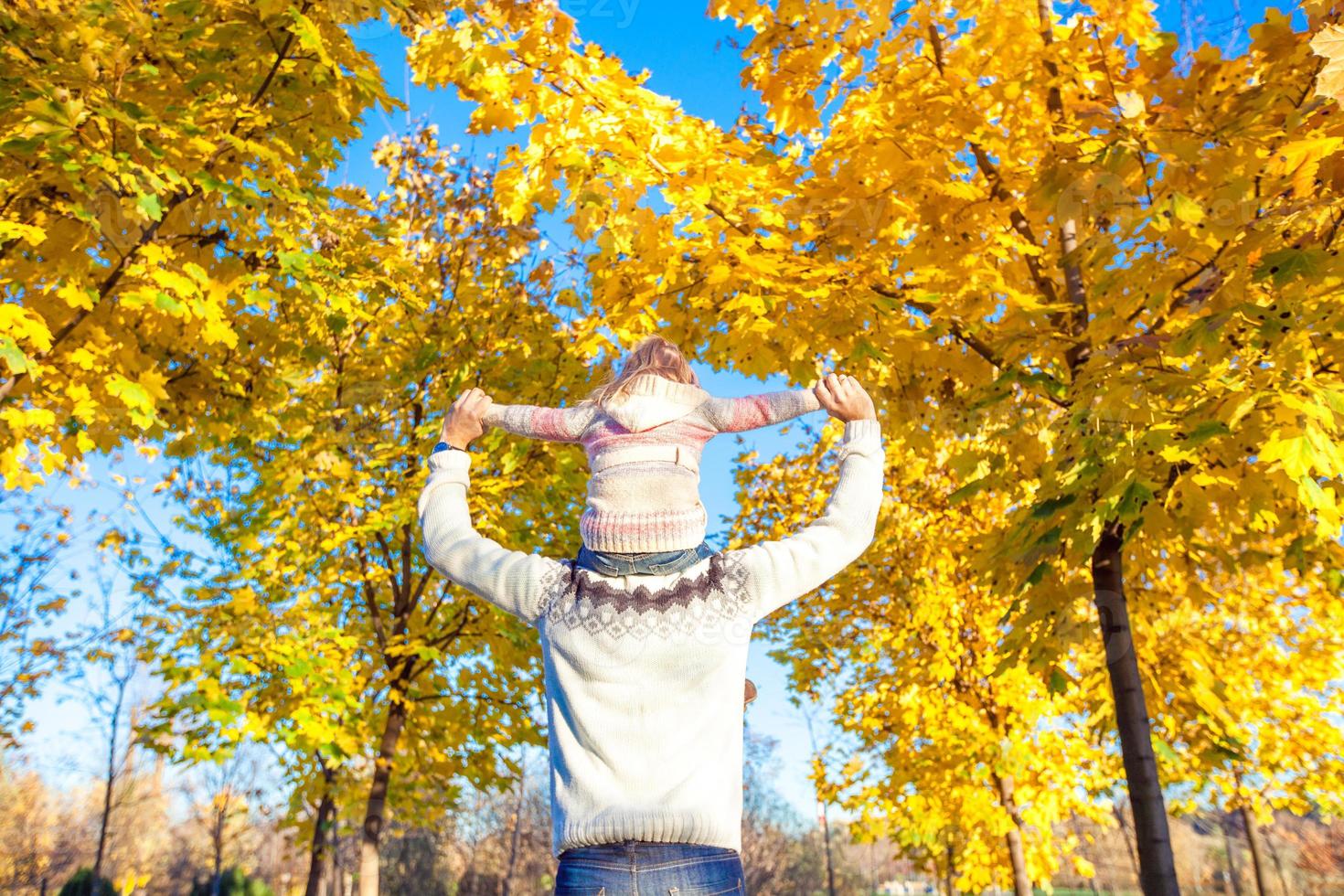 niña cabalgando sobre los hombros del padre en el parque de otoño foto