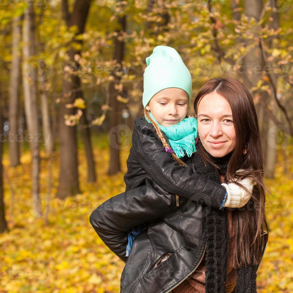 Happy mother and her cute daughter walking in yellow autumn forest on a warm sunny day photo
