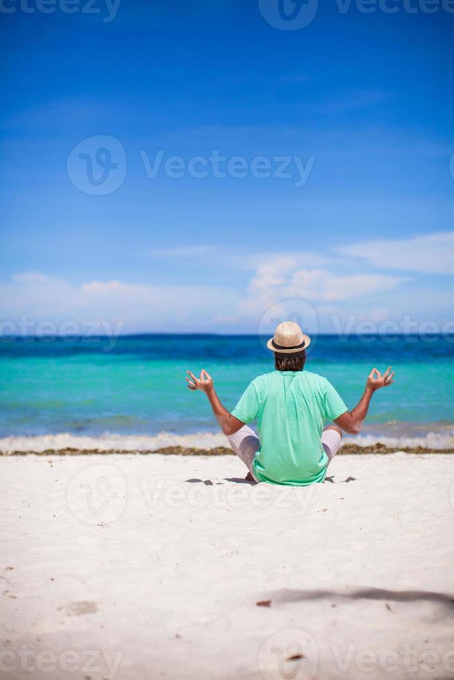 Young man sitting in lotus position on white tropical beach photo